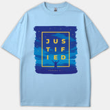 A light blue T-shirt with a navy graphic featuring stars, a silhouette raising hands, and yellow text reading JUSTIFIED along with the reference Romans 5:1.