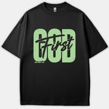 A black Christian t-shirt featuring large light-green block letters spelling GOD with black script text reading First across it, along with the Scripture reference Matthew 6:33.