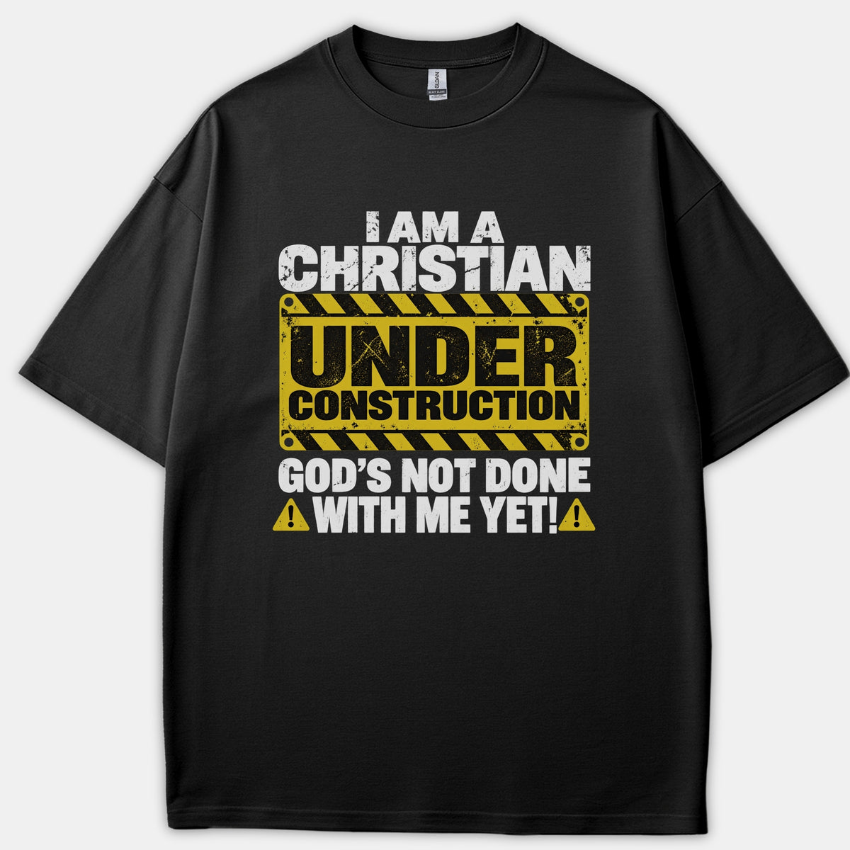A black t-shirt featuring a distressed graphic print reading 'I am a Christian under construction, God's not done with me yet!' with bold white lettering and a yellow caution sign.