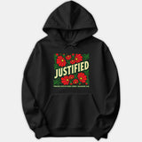A black hoodie featuring a graphic design with red flowers, green foliage, and the text JUSTIFIED THROUGH FAITH IN JESUS CHRIST with scripture reference Galatians 2:16.