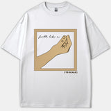 A white t-shirt featuring a framed illustration of a hand pinching a microscopic seed with the text 'faith like a' inside and '(TO SCALE)' printed below.