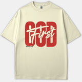 A beige Christian t-shirt featuring the phrase God First in bold red block font and off-white script, with the scripture reference Matthew 6:33 printed underneath.