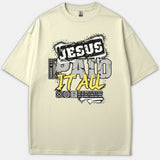 A beige graphic t-shirt featuring urban street-style typography that reads 'Jesus Paid It All' with a Romans 6:23 scripture reference in black, gray, and yellow distressed print.