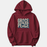 A dark red hoodie featuring a bold graphic with the text GRACE & PEACE in cream-colored block lettering set over a blue wave pattern.