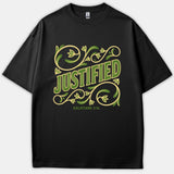 A black t-shirt featuring the word Justified surrounded by green and yellow floral scrollwork with the Bible reference Galatians 2:16 printed beneath.