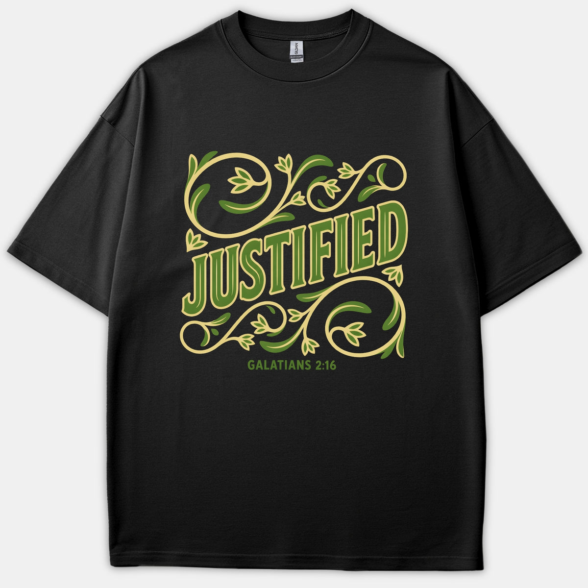 A black t-shirt featuring the word Justified surrounded by green and yellow floral scrollwork with the Bible reference Galatians 2:16 printed beneath.