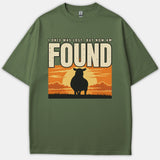 An olive green Christian t-shirt displaying the caption I ONCE WAS LOST BUT NOW AM FOUND above a silhouette of a sheep standing before a glowing sunset.