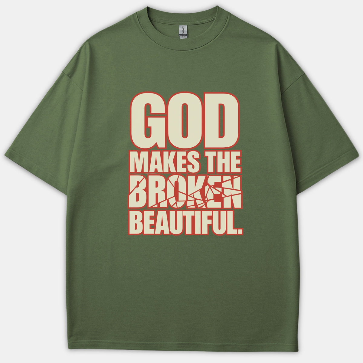 An olive green Christian T-shirt featuring bold text that reads 'GOD MAKES THE BROKEN BEAUTIFUL' in beige with a red outline and a cracked glass effect on the word broken.