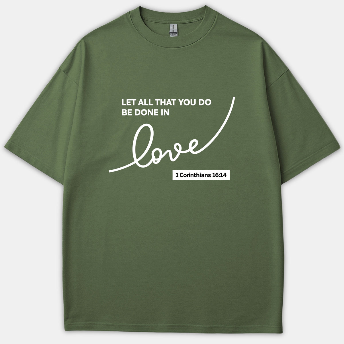 An olive green Christian t-shirt featuring the Bible verse 'Let all that you do be done in love' from 1 Corinthians 16:14 printed in white cursive and block lettering.
