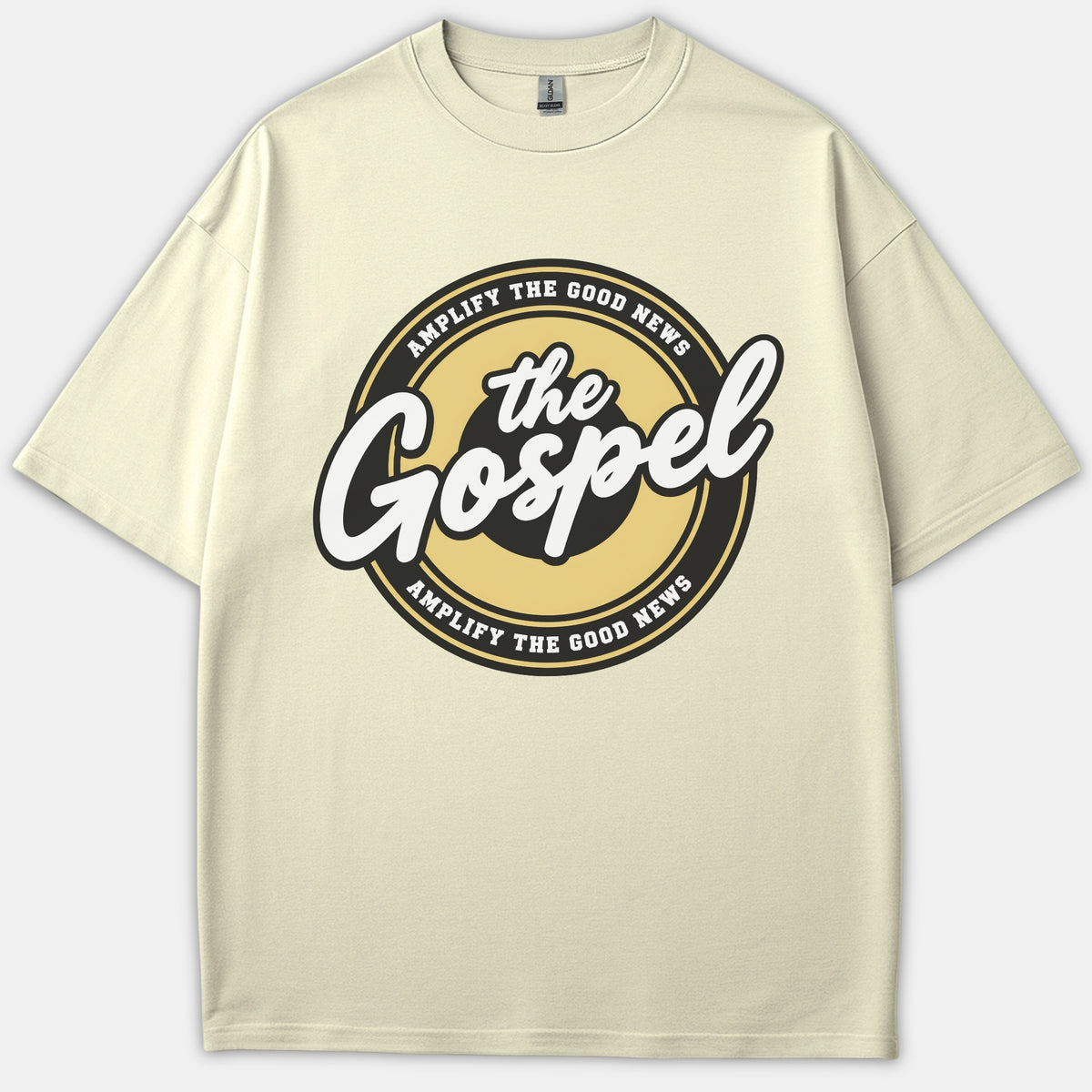A beige Christian t-shirt featuring a circular emblem graphic with the text 'the Gospel' in bold script and 'AMPLIFY THE GOOD NEWS' along the black and gold border.