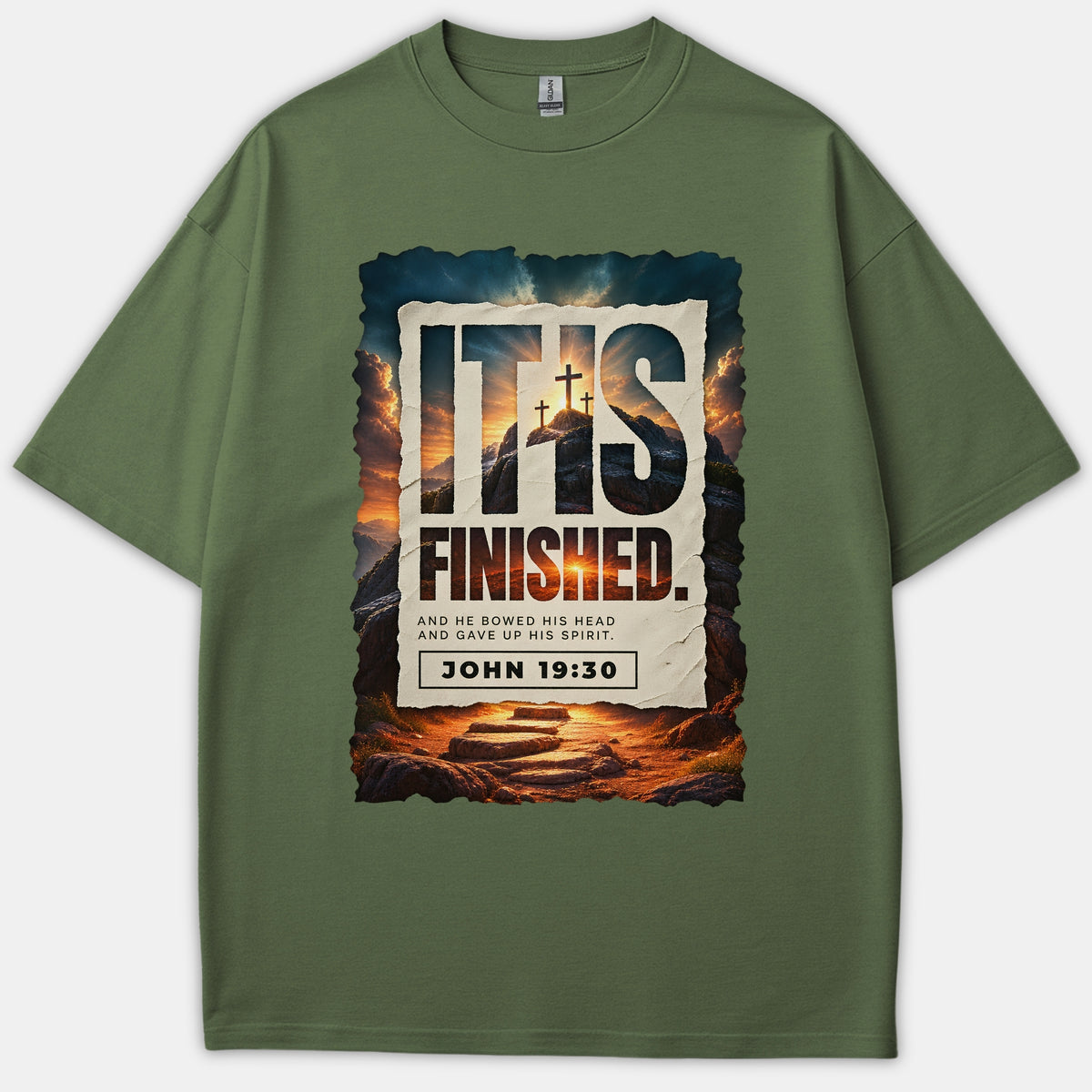 An olive green Christian t-shirt featuring a dramatic sunset graphic with three crosses, displaying the phrase 'IT IS FINISHED' and scripture reference John 19:30.