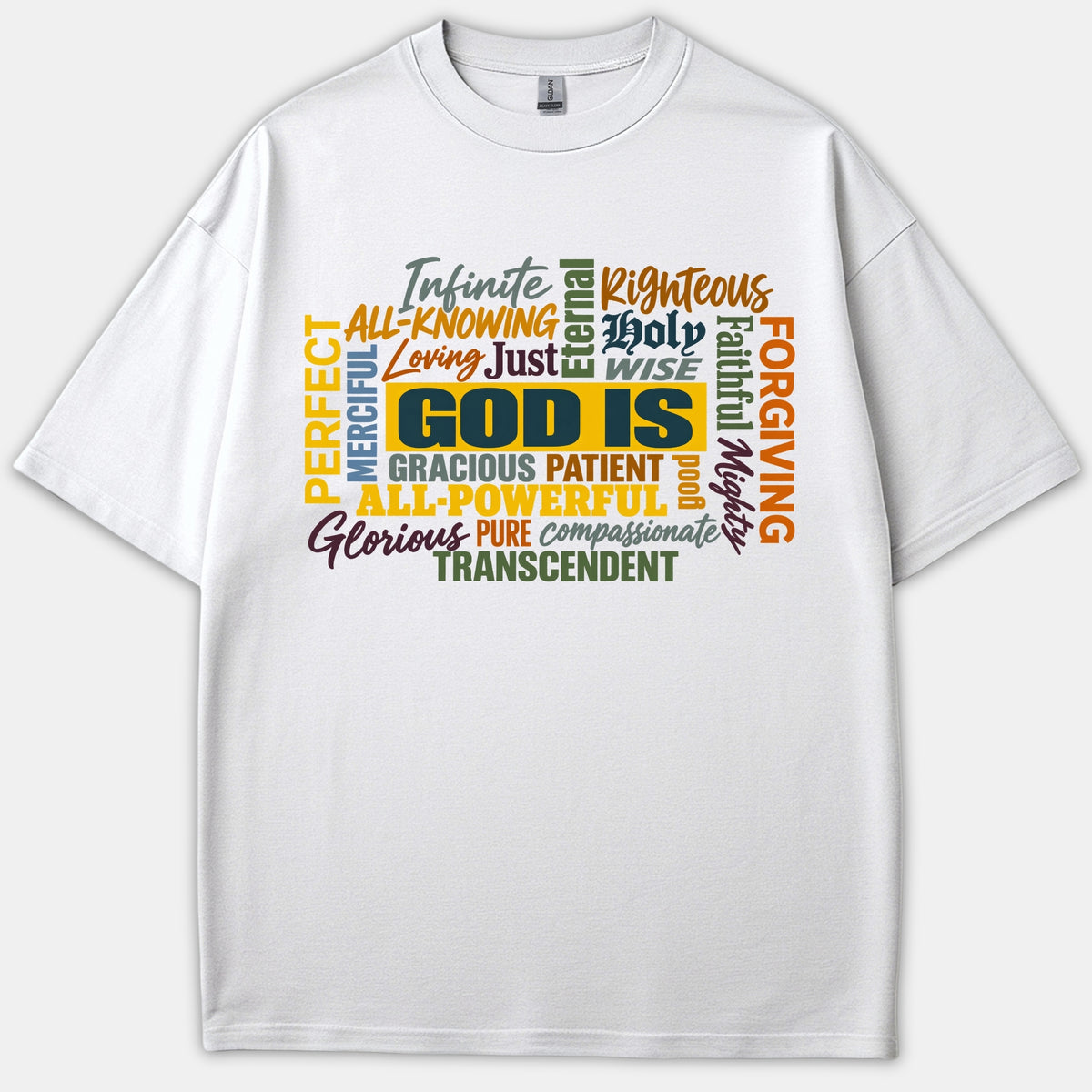 A white Christian T-shirt displaying a typography word cloud centered around 'GOD IS' surrounded by colorful attributes such as Righteous, Holy, Loving, and Faithful.