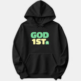 A black hoodie featuring bold graphic text that reads GOD 1ST in green and yellow lettering alongside a small Christian cross icon.