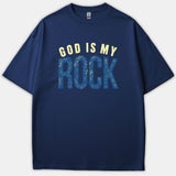 A navy blue Christian t-shirt featuring the phrase 'GOD IS MY ROCK' printed in light yellow and textured blue typography across the chest.