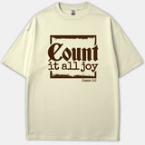 A beige t-shirt featuring a brown distressed square frame with the Bible verse phrase Count it all joy and James 1:2 printed in stylized text.