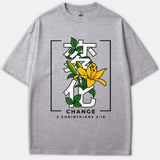 A gray t-shirt featuring a yellow lily flower and green leaves woven through white Japanese characters, with the word CHANGE and 2 Corinthians 3:18 printed below.