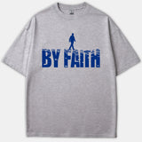 A gray Christian t-shirt featuring a blue graphic reading BY FAITH styled as water waves with a silhouette of a person walking on top.