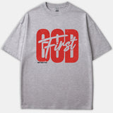 A gray Christian T-shirt featuring bold red text reading GOD layered with white script that says First, accompanied by the Bible verse Matthew 6:33 underneath.