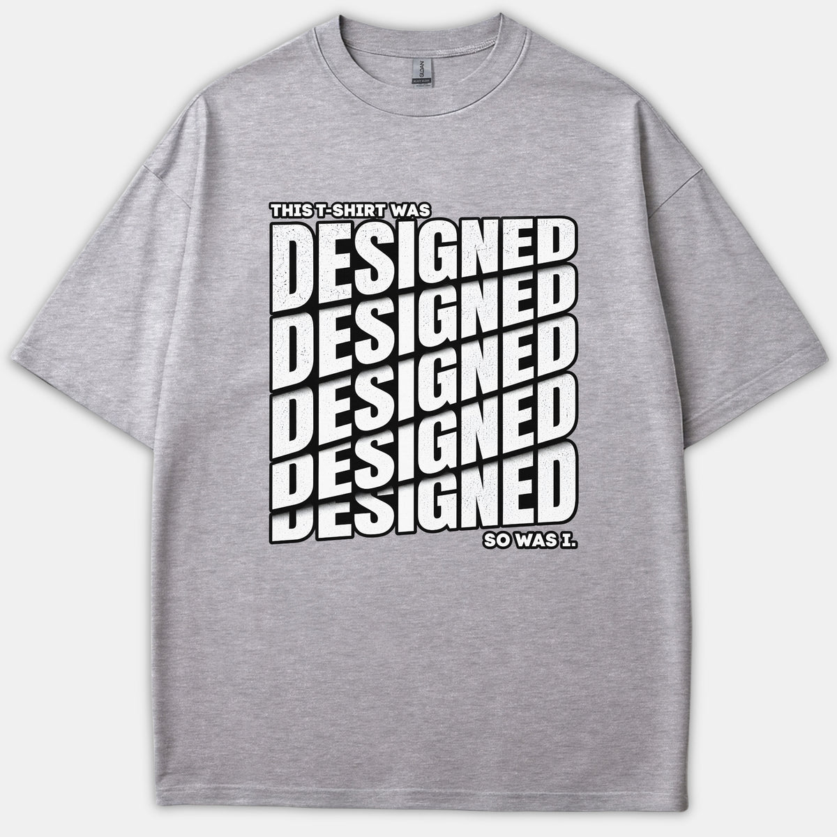 A heather gray t-shirt featuring bold black and white typography that reads 'THIS T-SHIRT WAS DESIGNED SO WAS I.' across the front.