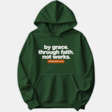 A dark green Christian hoodie featuring white text that reads 'by grace. through faith. not works.' above an orange box containing 'EPHESIANS 2:8-9'.