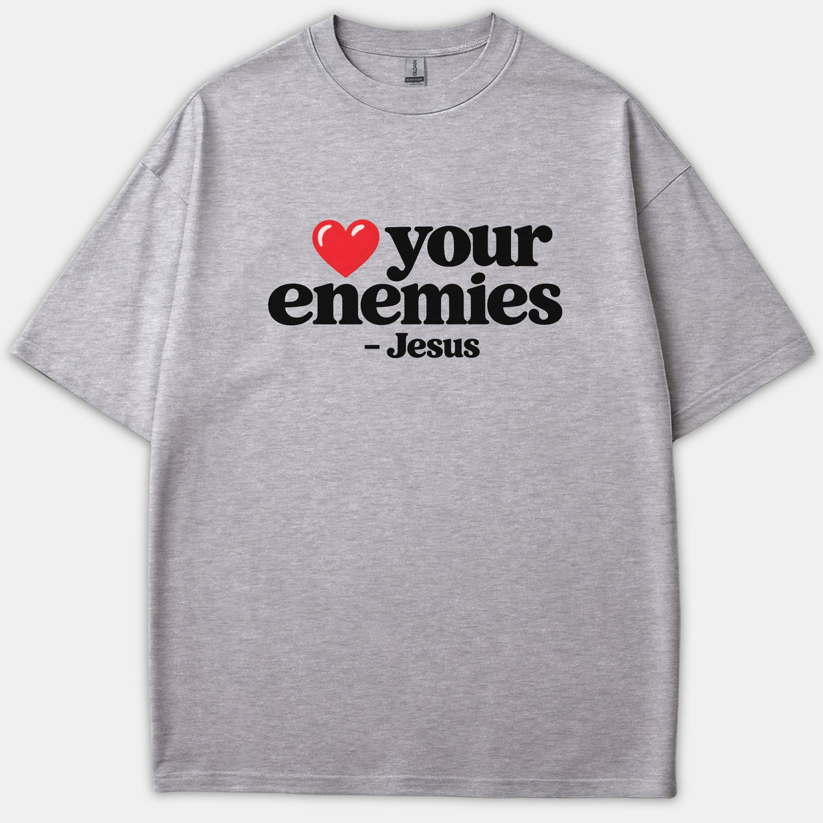 A heather gray t-shirt featuring a red heart icon followed by bold black text that reads 'your enemies - Jesus'.