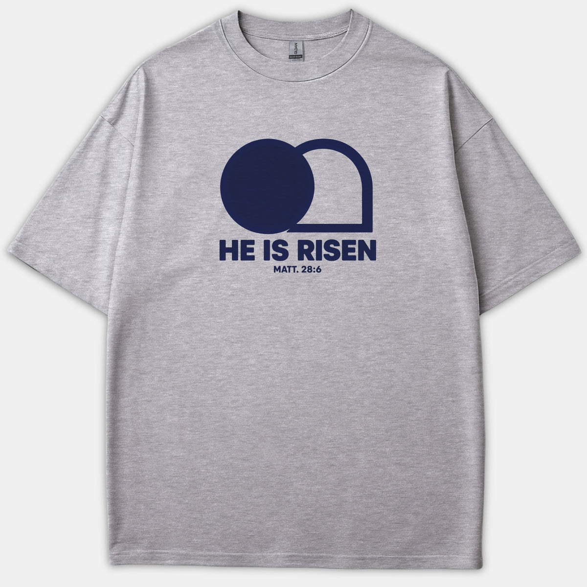 A gray Christian t-shirt featuring a navy graphic of an empty tomb with the text 'HE IS RISEN MATT. 28:6' printed on the chest.