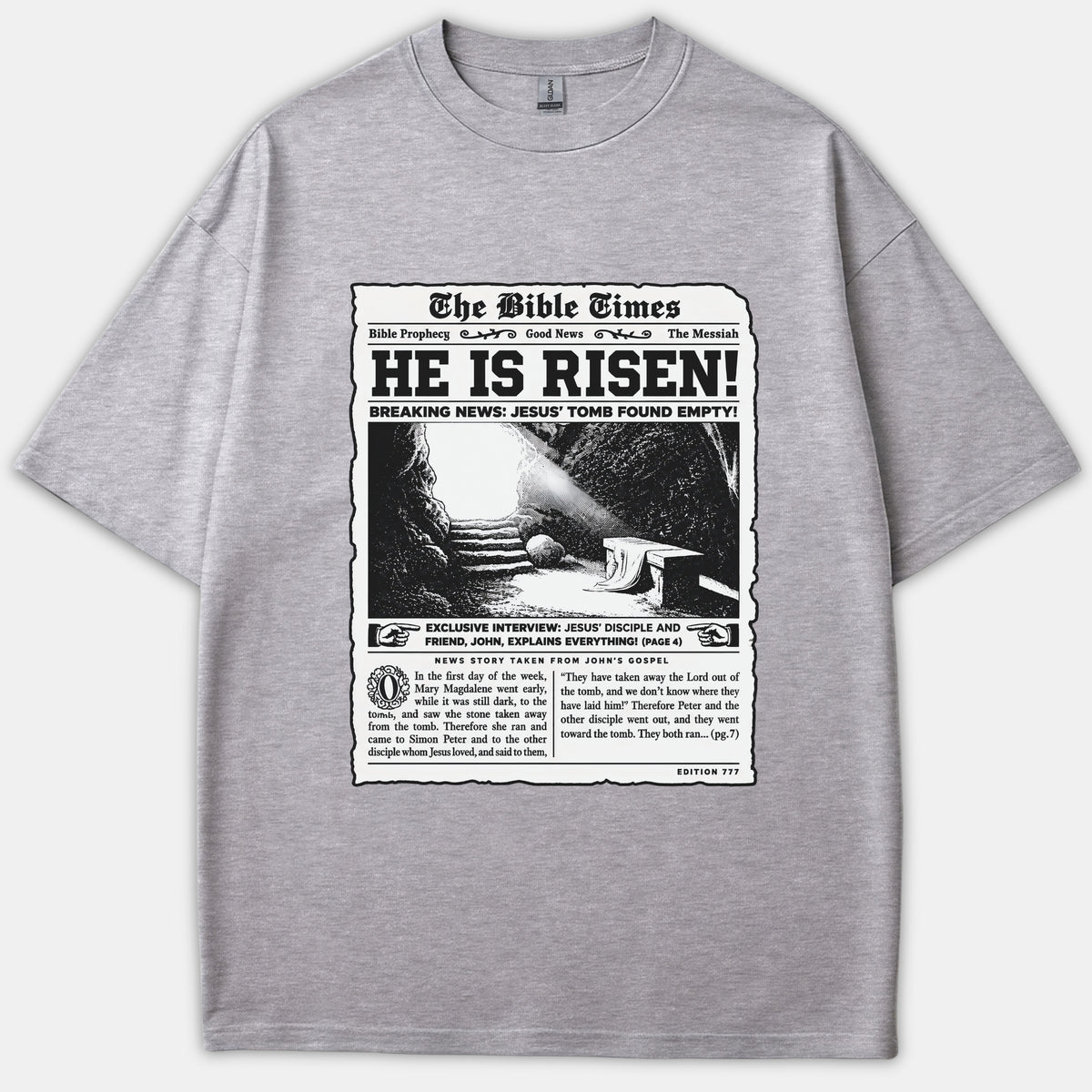 A heather gray t-shirt featuring a vintage newspaper front-page design titled 'The Bible Times' with the main headline 'HE IS RISEN!' and an illustration of Jesus' empty tomb.