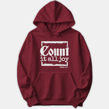 A red pullover hoodie featuring a white graphic print with the scripture phrase 'Count it all joy' and 'James 1:2' framed in a box.