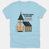 A light blue t-shirt featuring an illustration of a church building beside the text, 'Church isn’t a museum for good people. It’s a hospital for the broken.'