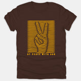 A brown t-shirt featuring a yellow optical illusion line art graphic of a peace sign with the phrase AT PEACE WITH GOD printed underneath.