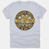 A light gray t-shirt featuring a circular navy and yellow graphic emblem with a cross, 'Man of God', and scripture text from Isaiah 54:17.