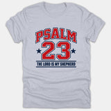A gray Christian T-shirt featuring an athletic varsity design that reads Psalm 23 and The Lord Is My Shepherd in bold red and navy blue typography.