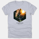 A light gray t-shirt featuring a geometric cube graphic filled with a radiant sunburst image and the text 'let there be light. (Genesis 1 v 3)' printed beneath.