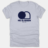 A gray Christian t-shirt featuring a navy graphic of an empty tomb above the words HE IS RISEN MATT. 28:6.