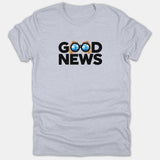 A light gray t-shirt featuring the phrase GOOD NEWS in bold black text, with binoculars reflecting a Christian cross against a blue sky replacing the double O's.