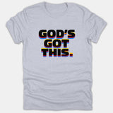 A light gray T-shirt featuring the Christian phrase GOD'S GOT THIS in bold black text with colorful red, yellow, and blue retro 3D shadows.