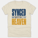 A beige t-shirt featuring bold typography that reads SYNCED WITH HEAVEN flanked by media and technology icons in navy blue, gray, and gold.