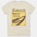 A beige Christian t-shirt featuring the word Covered above Psalm 91:4 scripture text and a detailed feather illustration on a vintage yellow parchment background.