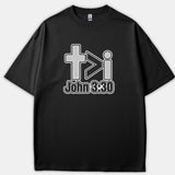 A black graphic T-shirt featuring a Christian design with a cross, a greater-than symbol, the letter i, and the Bible verse reference John 3:30 printed below.