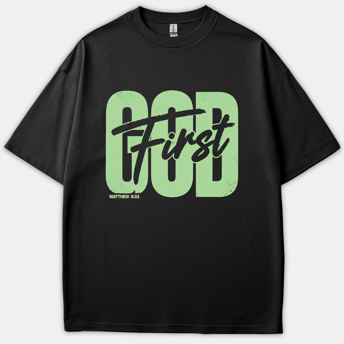 A black Christian t-shirt featuring large light-green block letters spelling GOD with black script text reading First across it, along with the Scripture reference Matthew 6:33.