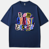 A navy blue t-shirt featuring a colorful collage graphic that reads 'I am CHRIST Encoded' in a cutout typography style paired with tech elements like a mouse and memory modules.