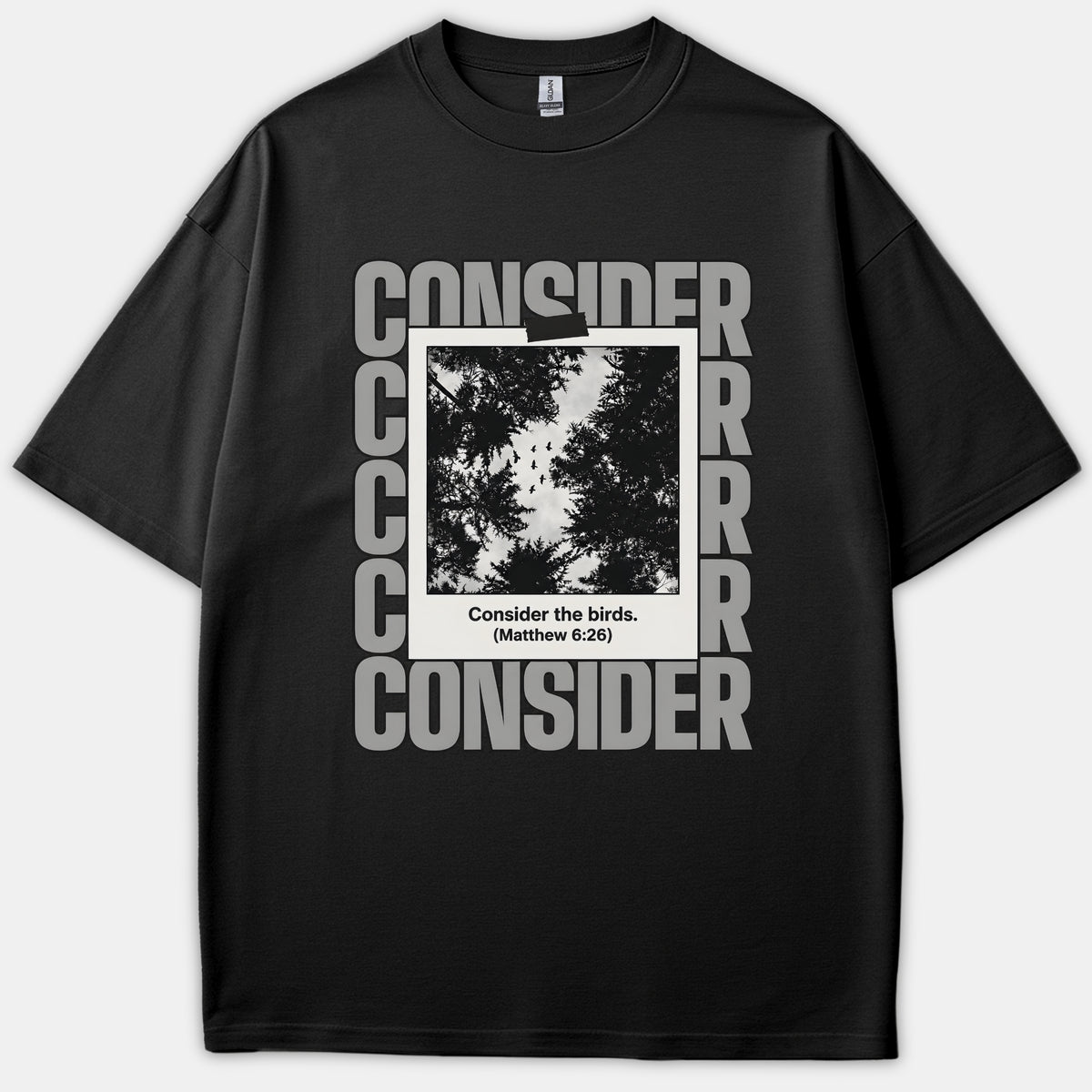 A black T-shirt featuring a polaroid picture of silhouette trees and birds surrounded by the word CONSIDER, with the text Consider the birds. (Matthew 6:26) written at the bottom.