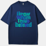 A navy blue t-shirt featuring the Christian phrase 'i know whom I have believed' in layered blue and green typography across the front.