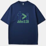 A navy blue t-shirt featuring a green and blue graphic reading + > i with the Scripture reference John 3:30 printed below.