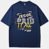 A navy blue Christian t-shirt featuring an urban graphic design with the words 'JESUS PAID IT ALL' and scripture reference Romans 6:23 styled in white, gray, and yellow fonts.
