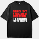 A black t-shirt featuring bold red and white text that reads, 'Church Isn't A Museum Of Good People. It's A Hospital For The Broken.'