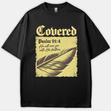 A black t-shirt featuring a vintage graphic with the text Covered Psalm 91:4 He will cover you with His feathers alongside a detailed feather illustration.