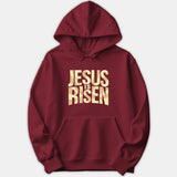 A dark red hoodie featuring the phrase 'JESUS IS RISEN' printed on the chest in a bold, geometric beige text design.