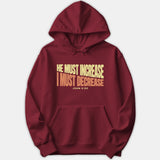A dark red hoodie featuring a bold graphic print that reads He Must Increase I Must Decrease John 3:30 in yellow and orange typography across the chest.