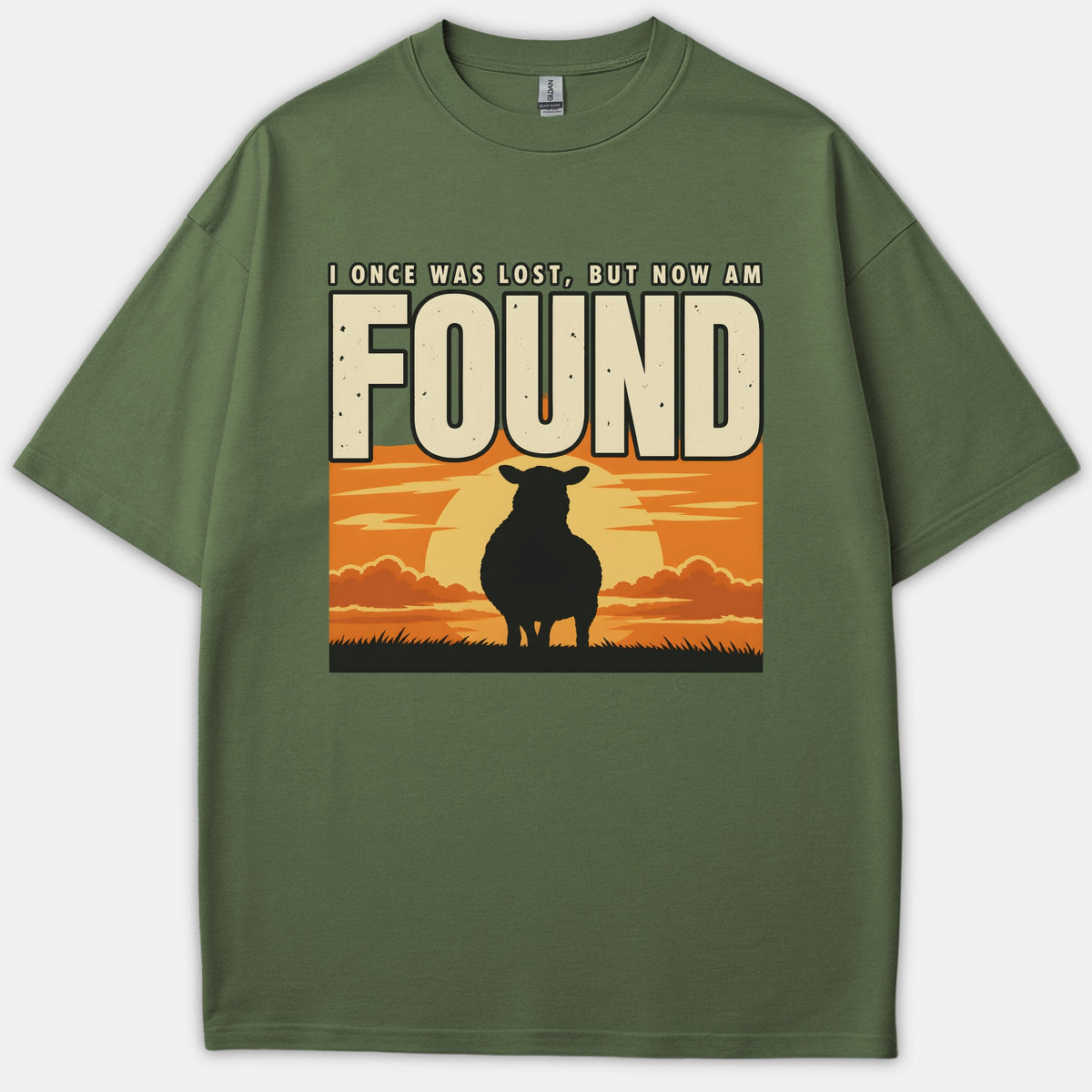 An olive green Christian t-shirt displaying the caption I ONCE WAS LOST BUT NOW AM FOUND above a silhouette of a sheep standing before a glowing sunset.